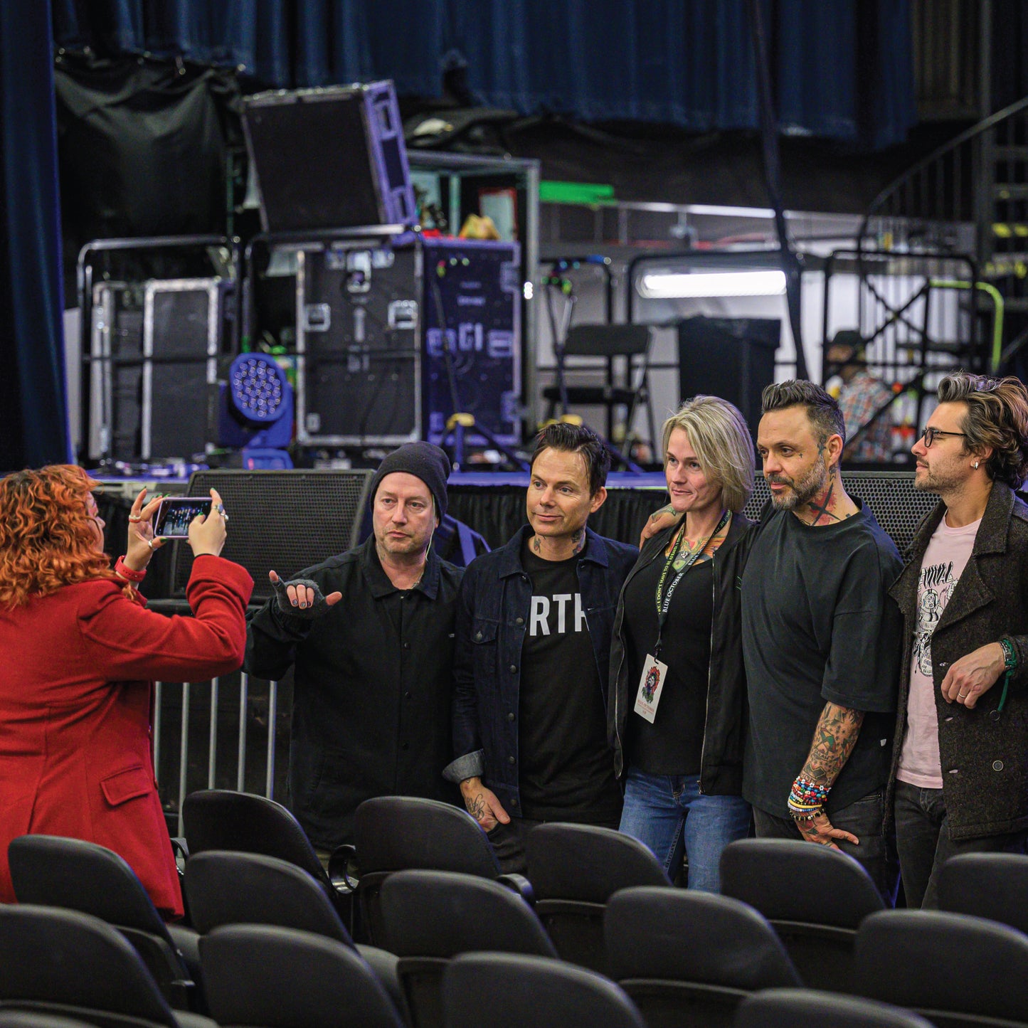 Group of people posing for a photo in an auditorium with stage equipment in the background - Blue October VIP Meet & Greet photo op