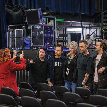 Group of people posing for a photo in an auditorium with stage equipment in the background - Blue October VIP Meet & Greet photo op